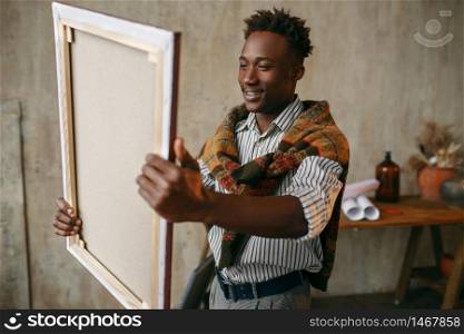 Smiling painter with canvas standing near the easel. Male artist draws at his workplace, creative master works in workshop. Smiling painter with canvas standing near easel