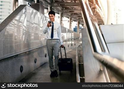 Smiling Passenger Businessman Using Mobile Phone while Walking with Suitcase in the Airport or Public Transportation Station. Lifestyle of Modern People. Full Length
