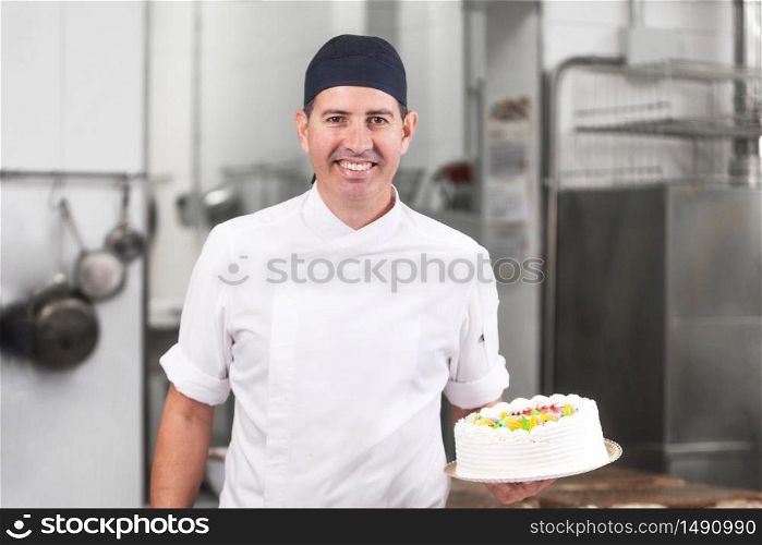 Smiling pastry Chef showing a cake in the pastry shop kitchen .. Smiling pastry Chef showing a cake