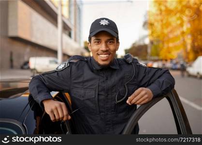 Smiling police officer in uniform poses at the patrol car. Policeman protect the law. Cop works on city street, order and justice control. Police officer in uniform poses at the patrol car