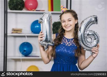 smiling portrait birthday girl holding numeral 16 foil silver balloon