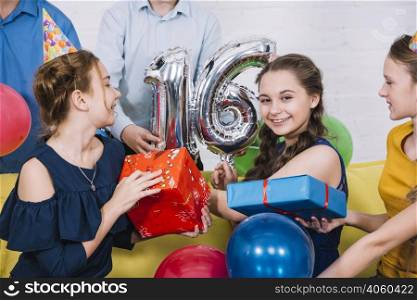 smiling portrait birthday girl with number 16 foil balloon presents