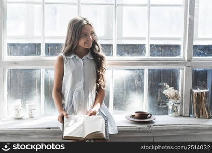 smiling portrait girl sitting window sill holding book looking away