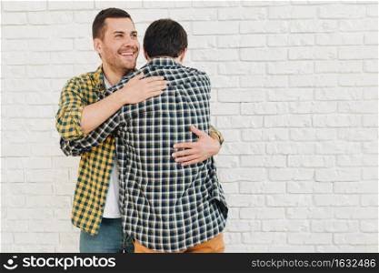 smiling portrait man giving hug his friend against white brick wall