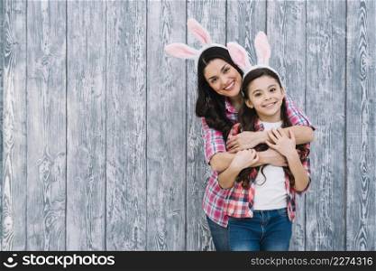 smiling portrait mother embracing her daughter from front wooden backdrop