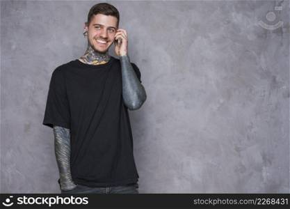 smiling portrait tattooed young man with pierced ears talking mobile phone