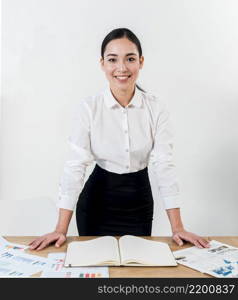 smiling portrait young businesswoman standing desk against white wall