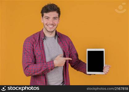 smiling portrait young man showing something digital tablet against orange background