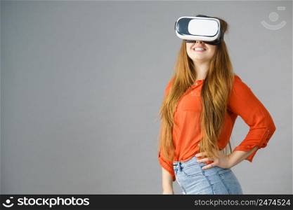 Smiling positive woman wearing virtual reality goggles headset, vr box. Connection, technology, new generation and progress concept. Studio shot on gray. Girl wearing virtual reality goggles.