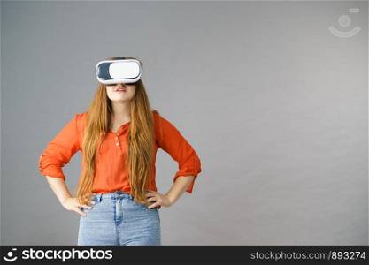 Smiling positive woman wearing virtual reality goggles headset, vr box. Connection, technology, new generation and progress concept. Studio shot on gray. Girl wearing virtual reality goggles.