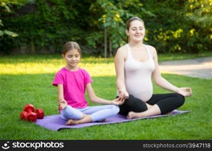 Smiling pregnant mother practicing yoga on grass at park