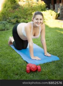 Smiling pregnant woman doing fitness on mat at park