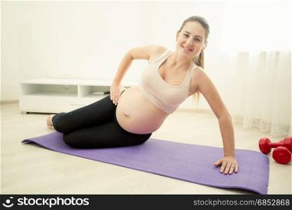 Smiling pregnant woman exercising on fitness mat at home