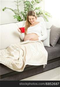 Smiling pregnant woman relaxing on sofa with cup of tea