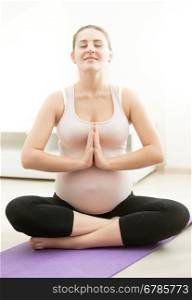 Smiling pregnant woman sitting on fitness mat and practicing yoga