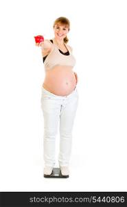 Smiling pregnant woman standing on weight scale and holding apple in hand isolated on white&#xA;