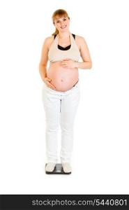 Smiling pregnant woman standing on weight scale and holding her belly isolated on white&#xA;