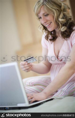 Smiling pregnant woman with laptop and credit card sitting on bed