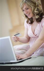 Smiling pregnant woman with laptop and credit card sitting on bed