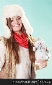 Smiling pretty cute woman holding little snowman. Attractive girl fur hat and white in studio on blue. Winter fashion.. Smiling cute woman with little snowman. Winter.