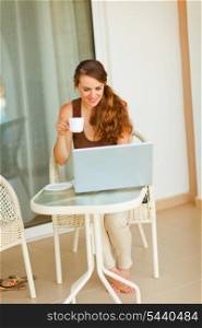 Smiling pretty woman having cup of tea and looking in laptop&#xA;