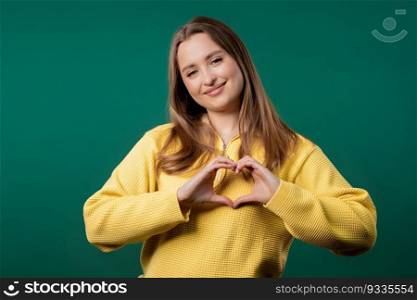 Smiling pretty woman showing sign of shape heart. Positive lady on green background. Women health, volunteering, charity donation, gratitude symbol, flirting concept. High quality . Smiling pretty woman showing sign shape heart. Positive lady on teal background