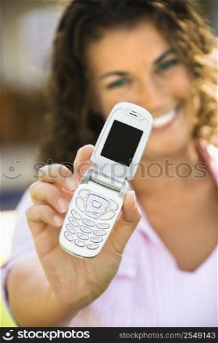 Smiling pretty young adult Caucasian brunette female holding cell phone towards viewer.