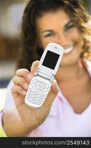 Smiling pretty young adult Caucasian brunette female holding cell phone towards viewer.