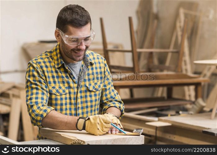 smiling professional male carpenter measuring wooden block with ruler
