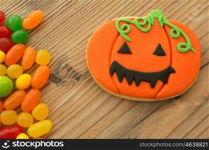 Smiling pumpkin cookie with many colorful candies on a wooden backgrund