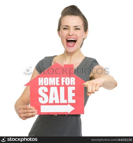Smiling realtor showing home for sale sign and pointing on you