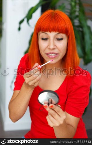 Smiling red hair girl using lipstick at home