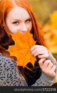 Smiling red-haired girl and maple leaves, close-up