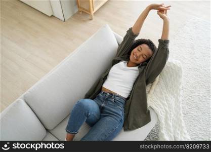 Smiling relaxed african american young girl stretching after afternoon nap lying on comfortable sofa at home. Happy lazy teen lady relaxing on cozy couch, enjoying calm weekend pause.. Relaxed african american young girl stretching after afternoon nap lying on cozy comfortable sofa