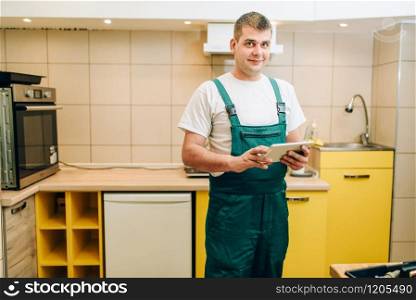 Smiling repairman in uniform holds laptop, handyman. Professional worker makes repairs around the house, home repairing service
