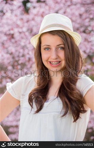 Smiling romantic girl with braces wearing hat against blossom tree
