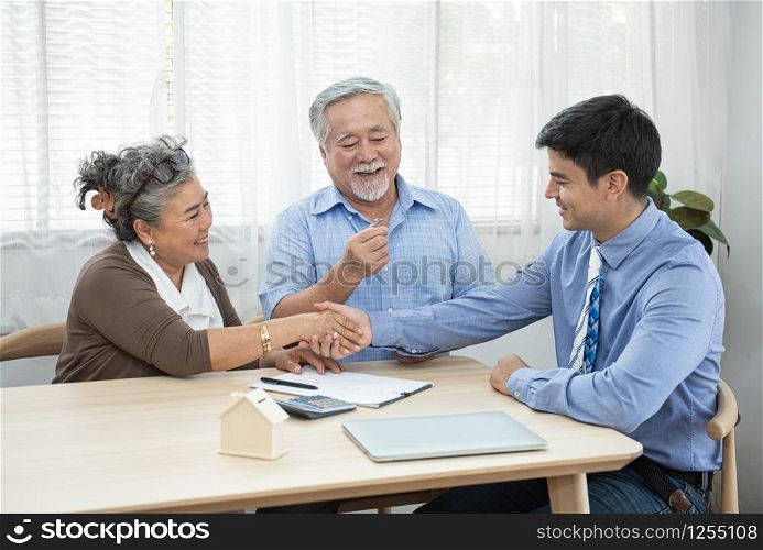 Smiling satisfied senior couple making sale purchase deal concluding contract hand get house key from real estate agent,happy older family and broker shake hands agreeing to buy new house at meeting.