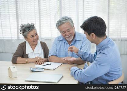 Smiling satisfied senior couple making sale purchase deal concluding contract hand get house key from real estate agent,happy older family and broker shake hands agreeing to buy new house at meeting.