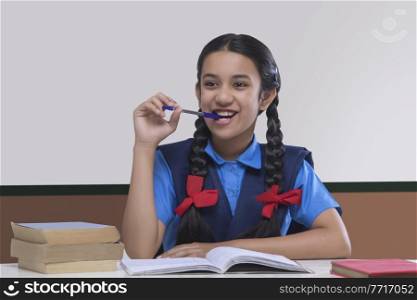 Smiling school girl holding pen in mouth