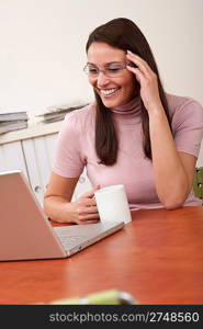 Smiling secretary with coffee and laptop sitting at office