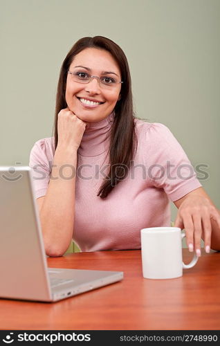 Smiling secretary with coffee and laptop sitting at office