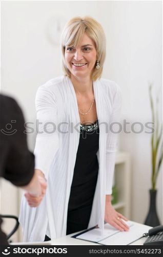 Smiling senior business woman shaking visitors hand