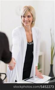 Smiling senior business woman shaking visitors hand