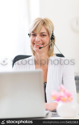 Smiling senior business woman with headset working on laptop