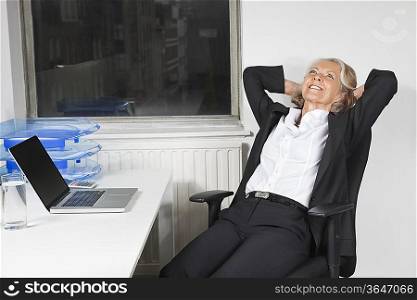 Smiling senior businesswoman relaxing at desk in office