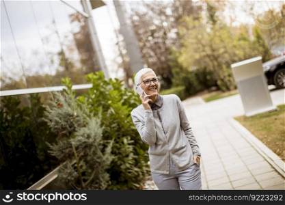 Smiling senior businesswoman talking on the phone while she is standing in front of an office building