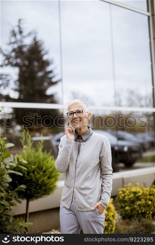Smiling senior businesswoman talking on the phone while she is standing in front of an office building