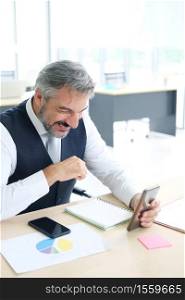 Smiling Senior Caucasian businessman relaxing with social media and online businesspeople on smartphone at workspace in office