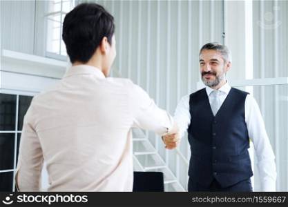 Smiling Senior Caucasian manager shaking hand with young Asain businessman after meeting and successful corporate in project