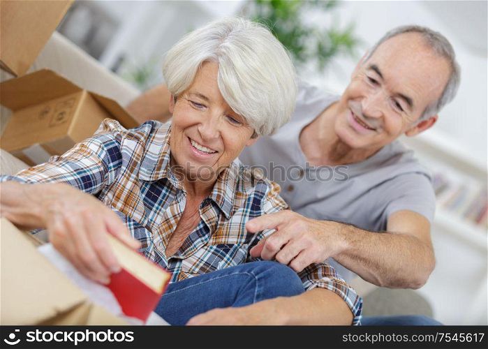 smiling senior couple unpacking carton boxes in living room